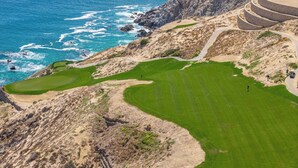 Un campo de golf frente al mar, con un sendero arenoso y una estructura circular de edificio.