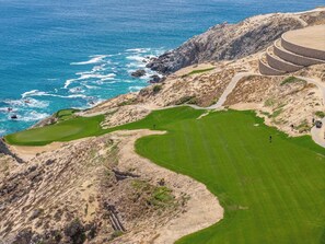 A coastal golf course with a view of the ocean, a sandy path, and a circular building structure. - CCV Quivira - Amazing 2BR Copala Condo w/ Ocean Views (Cabo San Lucas)