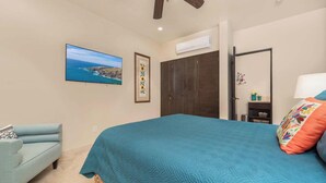 Un dormitorio con cama, una silla, armario, televisor y ventilador de techo.