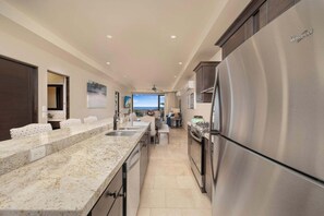 Una cocina moderna con refrigerador de acero inoxidable, encimeras de granito y vista al océano.