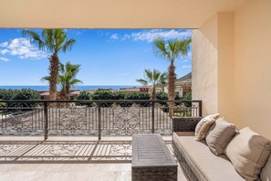 A balcony with a sofa and a table, overlooking a coastal area with palm trees and houses. - CCV Quivira - Amazing 2BR Copala Condo w/ Ocean Views (Cabo San Lucas)