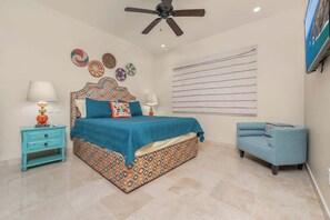 A bedroom with a bed, a nightstand, a chair, a ceiling fan, and wall decorations. - CCV Quivira - Amazing 2BR Copala Condo w/ Ocean Views (Cabo San Lucas)
