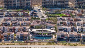 Zona residencial con varios edificios de apartamentos, una piscina central con zonas de descanso y un paisaje montañoso al fondo.