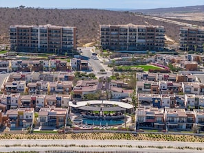 A residential area with multiple apartment buildings, a central swimming pool with lounge areas, and a hilly landscape in the background. - CCV Quivira - Amazing 2BR Copala Condo w/ Ocean Views (Cabo San Lucas)
