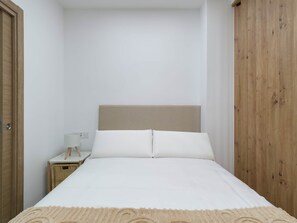 Ein Schlafzimmer mit einem Bett, einem Nachttisch, einer Lampe und einem Holzschrank.