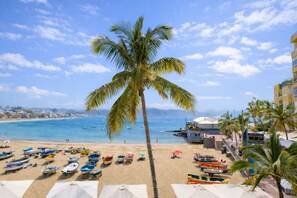 Ein Strand mit einer Palme, Booten, Sonnenschirmen und einem Gebäude mit einer digitalen Uhr.