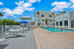 A pool area with lounge chairs, a covered seating area, and a building with multiple balconies. - Royal Mansions 3302 (Cape Canaveral)