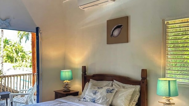 Une chambre avec un lit en bois, deux tables de chevet avec des lampes, un ventilateur de plafond, un climatiseur mural et une fenêtre donnant sur un paysage verdoyant.