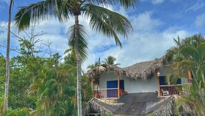 Une piscine dotée d’une structure surmontée d’un toit de chaume, entourée d’une végétation luxuriante et de palmiers.