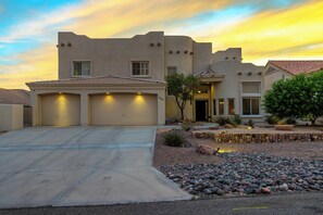 A modern two-story house with a garage, a driveway, and a landscaped front yard with rocks and plants. - Spacious 5-bedroom house in serene Lake Havasu with pool, and Lake view (Lake Havasu City)