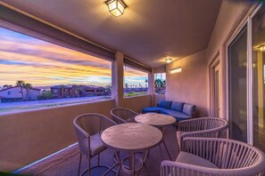 A balcony with wicker furniture, a sofa, and a view of a residential area during sunset. - Spacious 5-bedroom house in serene Lake Havasu with pool, and Lake view (Lake Havasu City)