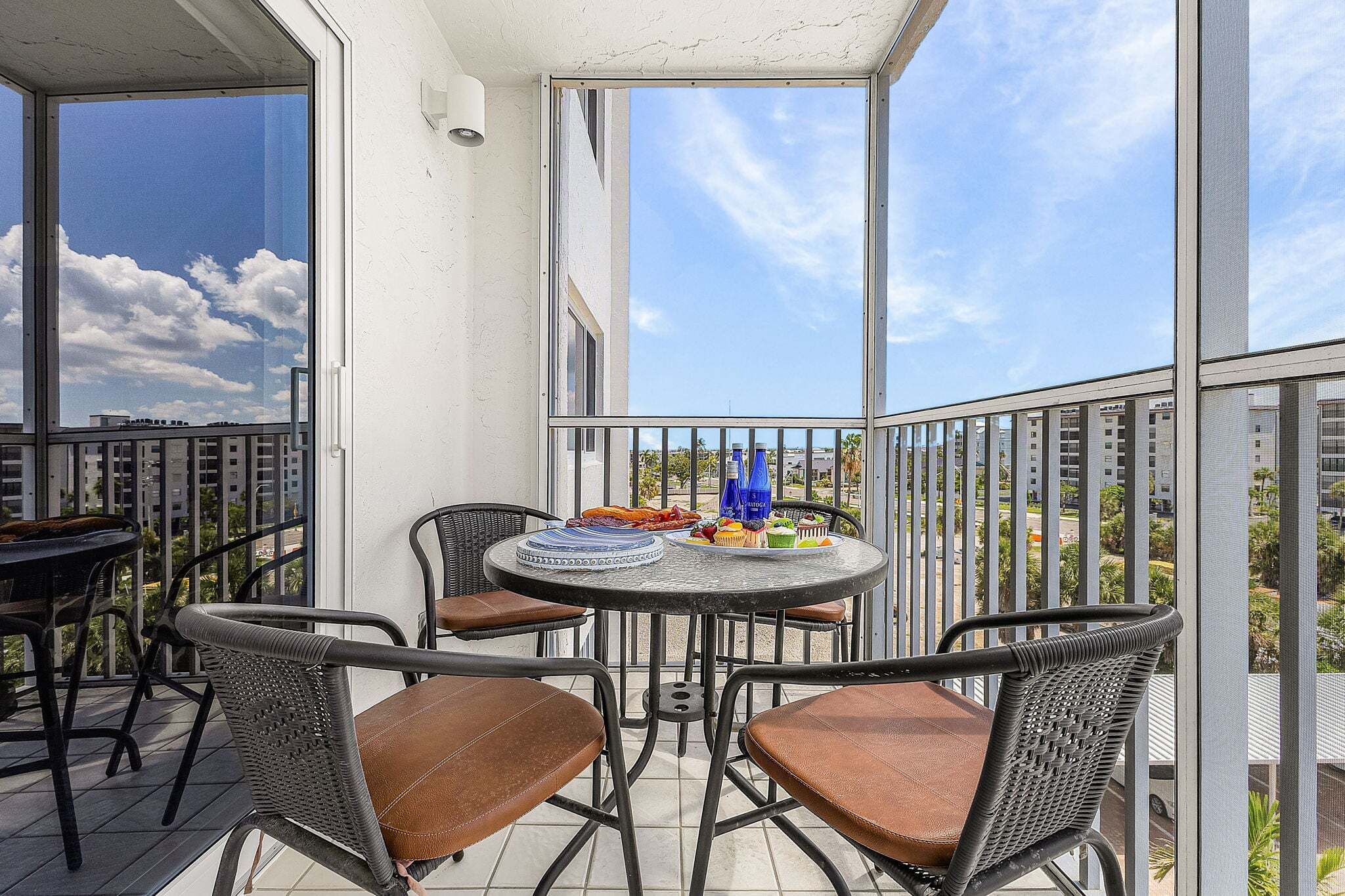 A balcony with a round table, four chairs, and a view of buildings and trees.