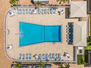 Eine Vogelperspektive zeigt einen Swimmingpool mit Liegestühlen und Sonnenschirmen, umgeben von einer gefliesten Terrasse und Palmen.