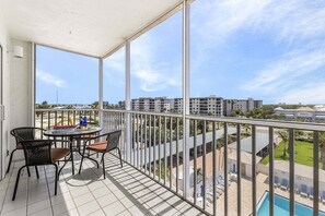 Un balcon avec une table et des chaises, une piscine et une vue sur les bâtiments environnants.