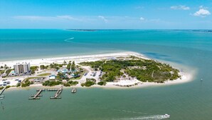 An aerial view of a coastal resort with a marina, a sandy beach, and a small island with dense vegetation. - Beachfront Escape with Pool & Island Fun Steps from the Sand - Sand Caper 509 - Roelens (Fort Myers Beach)
