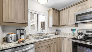A kitchen with wooden cabinets, a stainless steel dishwasher, a microwave, and a stove. - Beachfront Escape with Pool & Island Fun Steps from the Sand - Sand Caper 509 - Roelens (Fort Myers Beach)