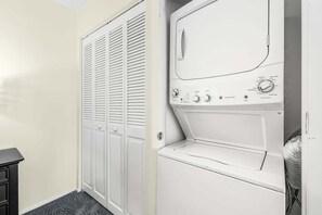 Una lavandería con lavadora y secadora blancas, una puerta blanca con paneles verticales y un armario negro.
