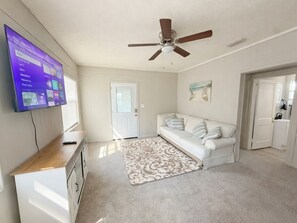 A room with a ceiling fan, a white sofa, a TV mounted on the wall, and a door leading to another room.