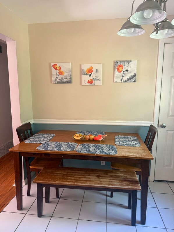 A dining area with a wooden table, bench, and chairs. There are three paintings on the wall above the table.