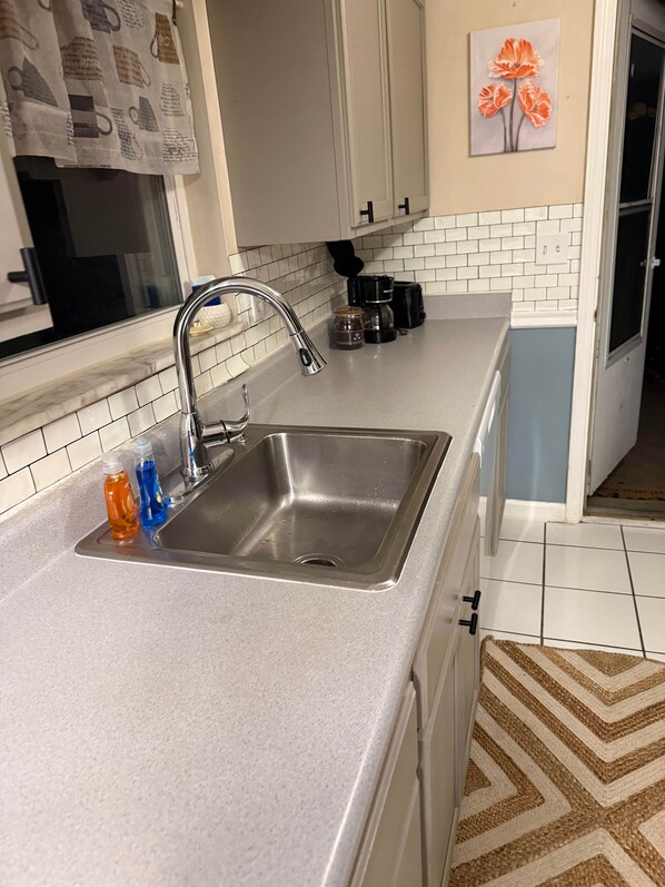 A kitchen with a stainless steel sink, white cabinets, a tiled backsplash, and a coffee maker.