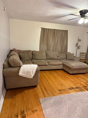 A living room with a sectional sofa, a ceiling fan, and a window with curtains.