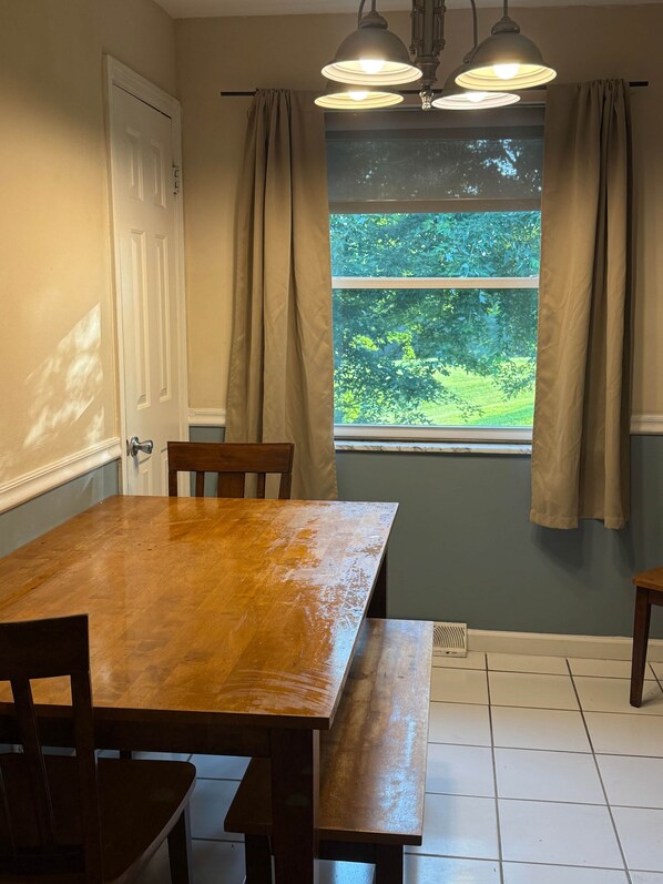 Een eetgedeelte met een houten tafel, stoelen en een raam met gordijnen.