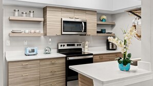 Eine moderne Küche mit Mikrowelle, Herd und Toaster. Holzschränke, eine weiße Arbeitsplatte und eine Vase mit Blumen sind zu sehen.
