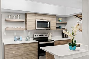 A modern kitchen with a microwave, stove, and toaster. There are wooden cabinets, a white countertop, and a vase with flowers. - Sandpiper Towers 512 (Satellite Beach)