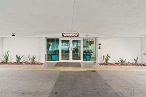 A hotel entrance with a sign reading 'Sandpiper Towers,' glass doors, potted plants, and a paved driveway. - Sandpiper Towers 512 (Satellite Beach)