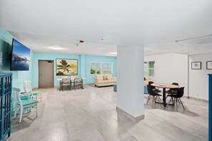 A spacious room with a large window, a sofa, and a dining table with chairs. - Sandpiper Towers 512 (Satellite Beach)