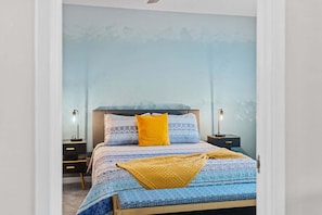 A bedroom with a bed, two bedside tables, and a wall with a mountain pattern. - Sandpiper Towers 512 (Satellite Beach)