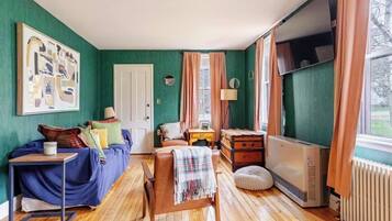 A room with a bed, a desk, a chair, a radiator, and a window with curtains.