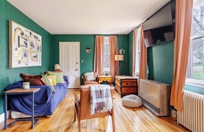 A room with a bed, a desk, a chair, a radiator, and a window with curtains.