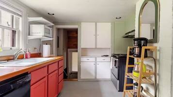 A compact kitchen with a sink, microwave, and stove, a red dishwasher, and a wooden ladder shelf.