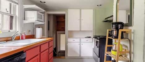 Cocina compacta con lavamanos, microondas y estufa, un lavavajillas rojo y una estantería de madera con escalera.