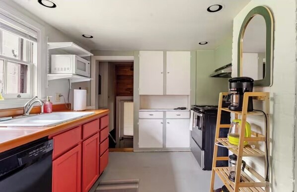 A compact kitchen with a sink, microwave, and stove, a red dishwasher, and a wooden ladder shelf.