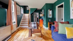 Una habitación con una escalera, una cama con almohadones de colores, una mesita con un control remoto y un radiador.