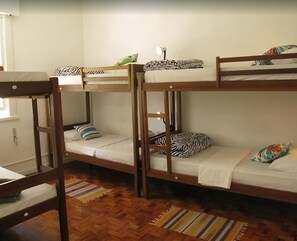 Dormitori amb lliteres de fusta, roba de llit blanca i catifes ratllades.