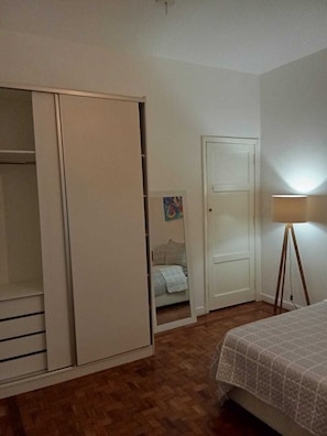 Un dormitori amb un armari, un llit, una làmpada de peu i una porta.