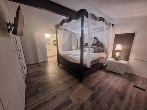 A four-poster canopy bed with a bedside table and lamp, wooden flooring, and a wardrobe.