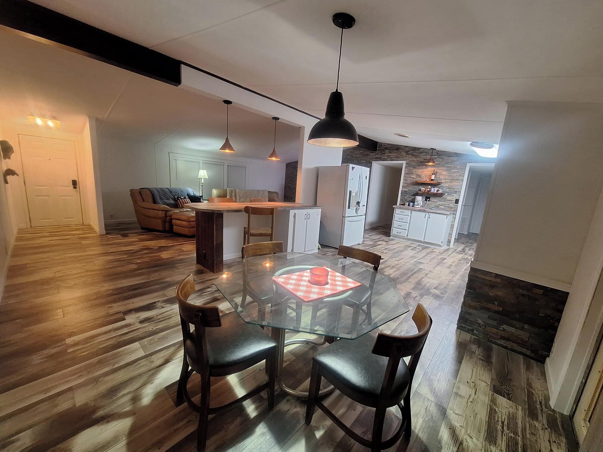 A modern kitchen with a central island, wooden flooring, and pendant lighting.