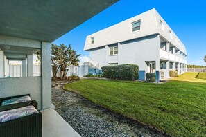 Un bâtiment moderne à deux étages, doté d’un toit plat, d’un patio couvert aménagé avec des meubles en osier et d’une pelouse bien entretenue.