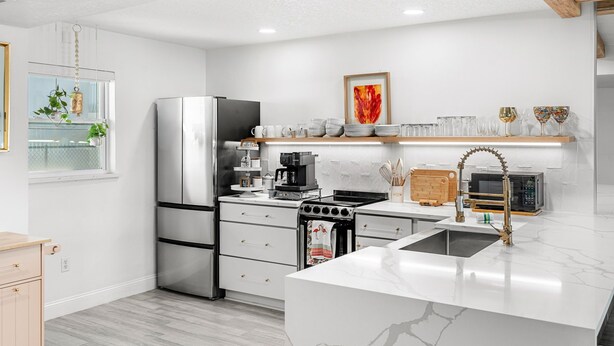 A modern kitchen with stainless steel appliances, a marble countertop, and a wooden ceiling beam. - Seabreakers 2 (Satellite Beach)