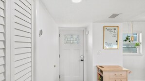 A hallway with a white door, a small window with a plant, and a wooden cabinet with drawers. - Seabreakers 2 (Satellite Beach)