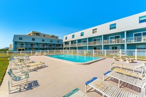 A pool area with lounge chairs and a building with multiple balconies. - Seabreakers 2 (Satellite Beach)