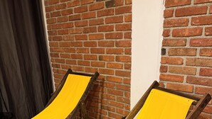 Deux fauteuils de couleur jaune sont placés contre un mur de briques dans une pièce dont le sol est recouvert de planches de bois.