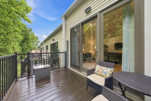 Un espace extérieur abrité doté d'une terrasse en bois, de meubles en osier et d'une porte-fenêtre coulissante donnant sur un espace intérieur.
