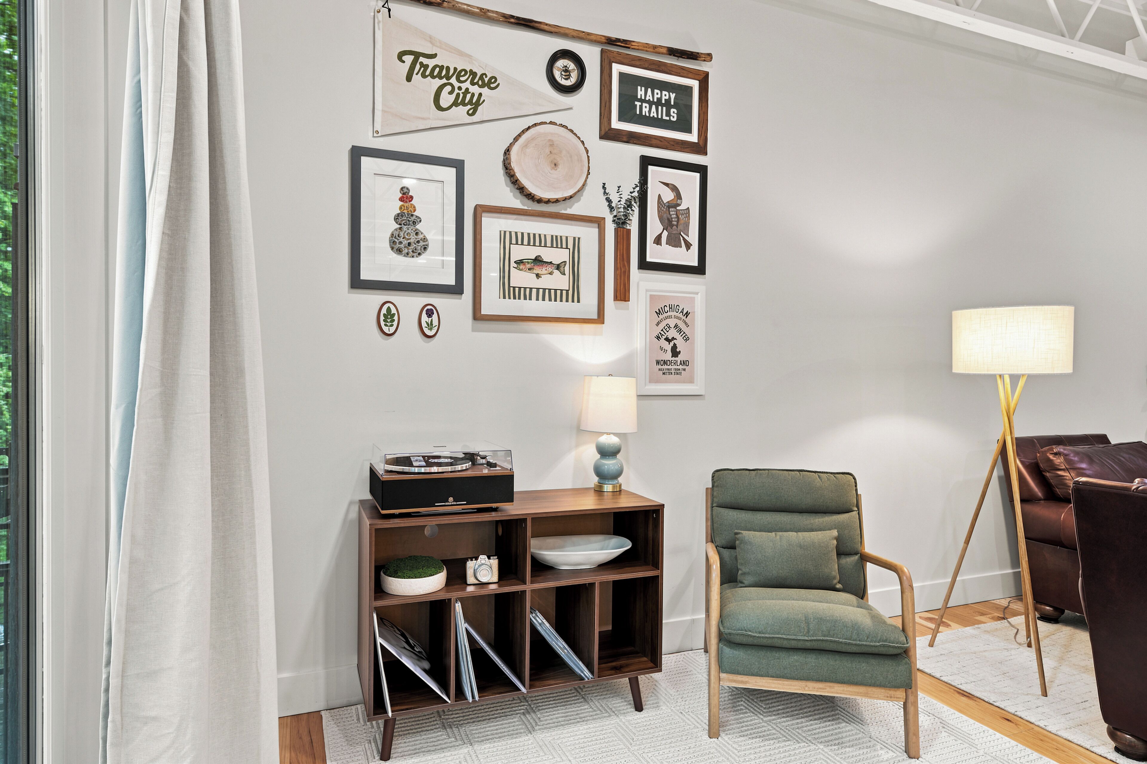 Una habitación con una estantería de pared que exhibe varios objetos enmarcados, un sillón verde, una lámpara y un sofá de cuero.