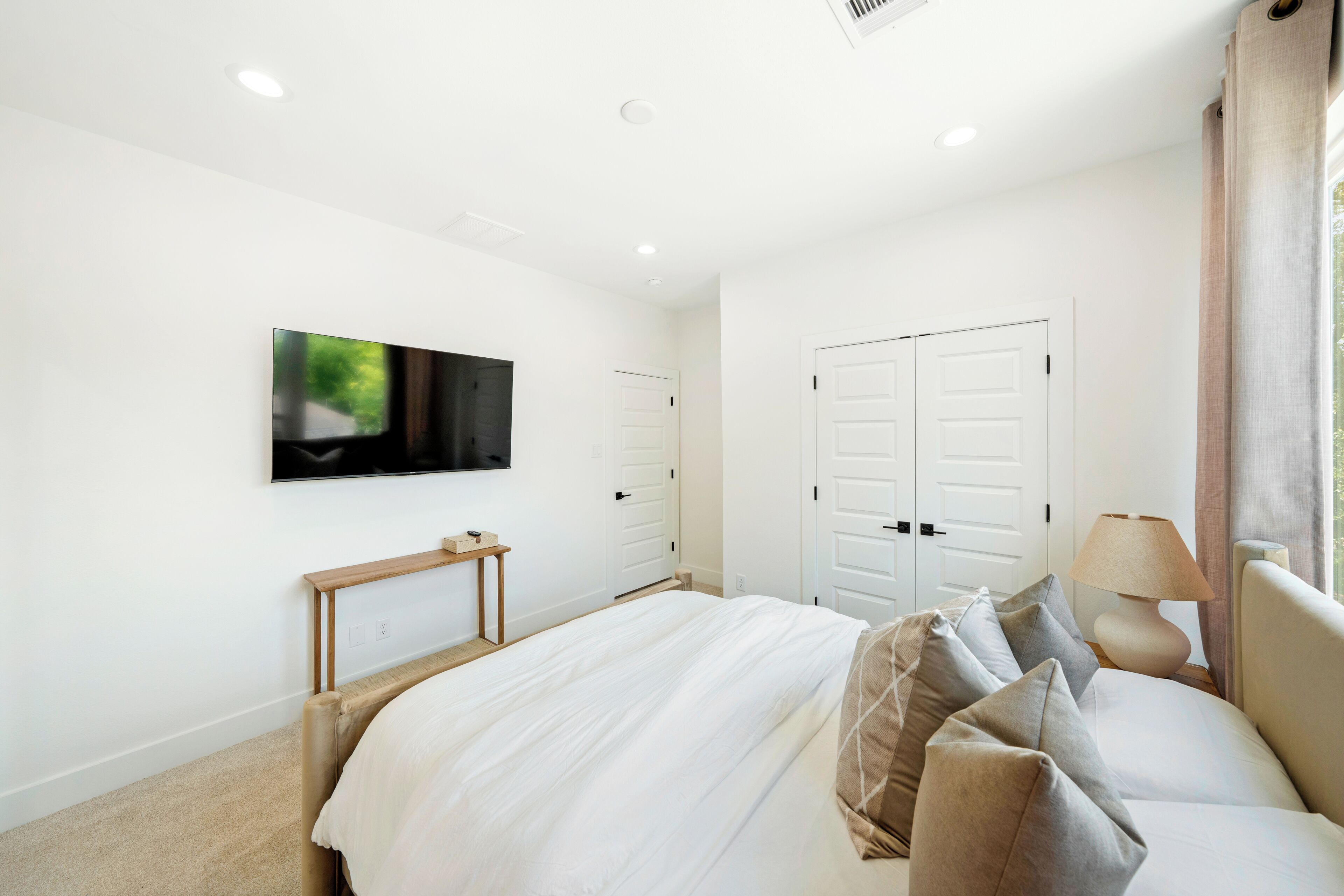 A bedroom with a bed, a TV mounted on the wall, a door, and a window with curtains.