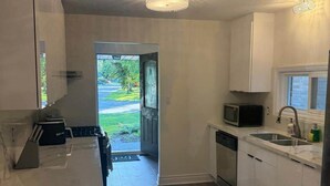 A modern kitchen with white cabinets, a microwave, a sink, and a dishwasher. There is a door leading to a garden. - Executive Parkside Retreat in Heart of Unionville (Markham)